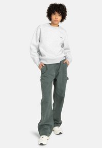 Sudadera gris claro con cuello redondo y puños acanalados, combinada con pantalones de pierna ancha verde oscuro. Los zapatos son blancos con detalles en color.