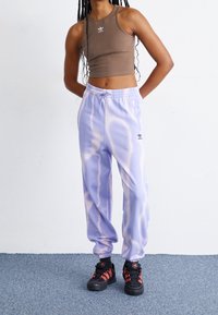 Brun kortärmad topp, lila tie-dye sweatpants med elastiska mudd, och svarta sneakers med röda accenter och texturerade sula.