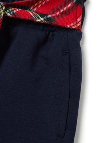 Marineblauwe gebreide broek met een elastische tailleband en een zichtbare zijzak, gecombineerd met een rood-groen geruit stof aan de bovenkant.