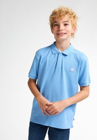 Světlomodrý polo tričko vyrobené z bavlny, s límečkem, krátkými rukávy a malou vyšitou značkou na hrudi.