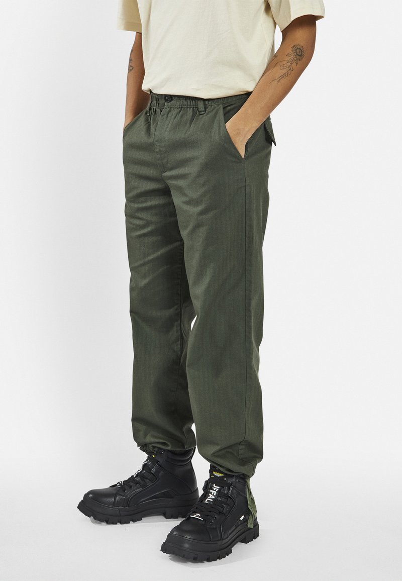 Olive green pants with an elastic waistband, side pockets, and a straight-leg design, paired with black lace-up boots. Textured fabric finish.
