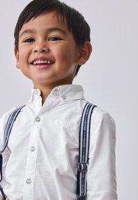 A boy in a white button-up shirt features embroidered "BAKER" and navy-blue suspenders with a repeating "BAKER" pattern.
