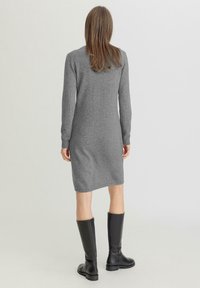 Abito lavorato a maglia grigio con scollatura rotonda e maniche lunghe, di lunghezza media, abbinato a stivali alti in pelle nera. Texture piatta, design casual.