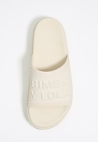 Krémová šľapka s hrubým remienkom s embosovaným nápisom "BIMBA Y LOLA". Vyrobená z mäkkého materiálu, s tvarovanou stielkou.