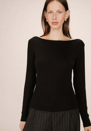 Haut noir à manches longues avec un large col, fabriqué en tissu extensible ; design ajusté. Porté avec un pantalon taille haute à rayures.