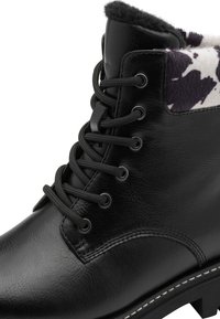 Bottines en cuir noir avec un accent en imprimé vache gris et blanc. Présentent des lacets ronds passant par des œillets en métal et une semelle en caoutchouc texturée.