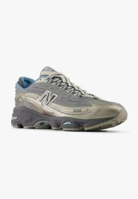 Gray athletic sneakers with a mesh upper and smooth synthetic accents. Features a prominent "N" logo and cushioned sole design.