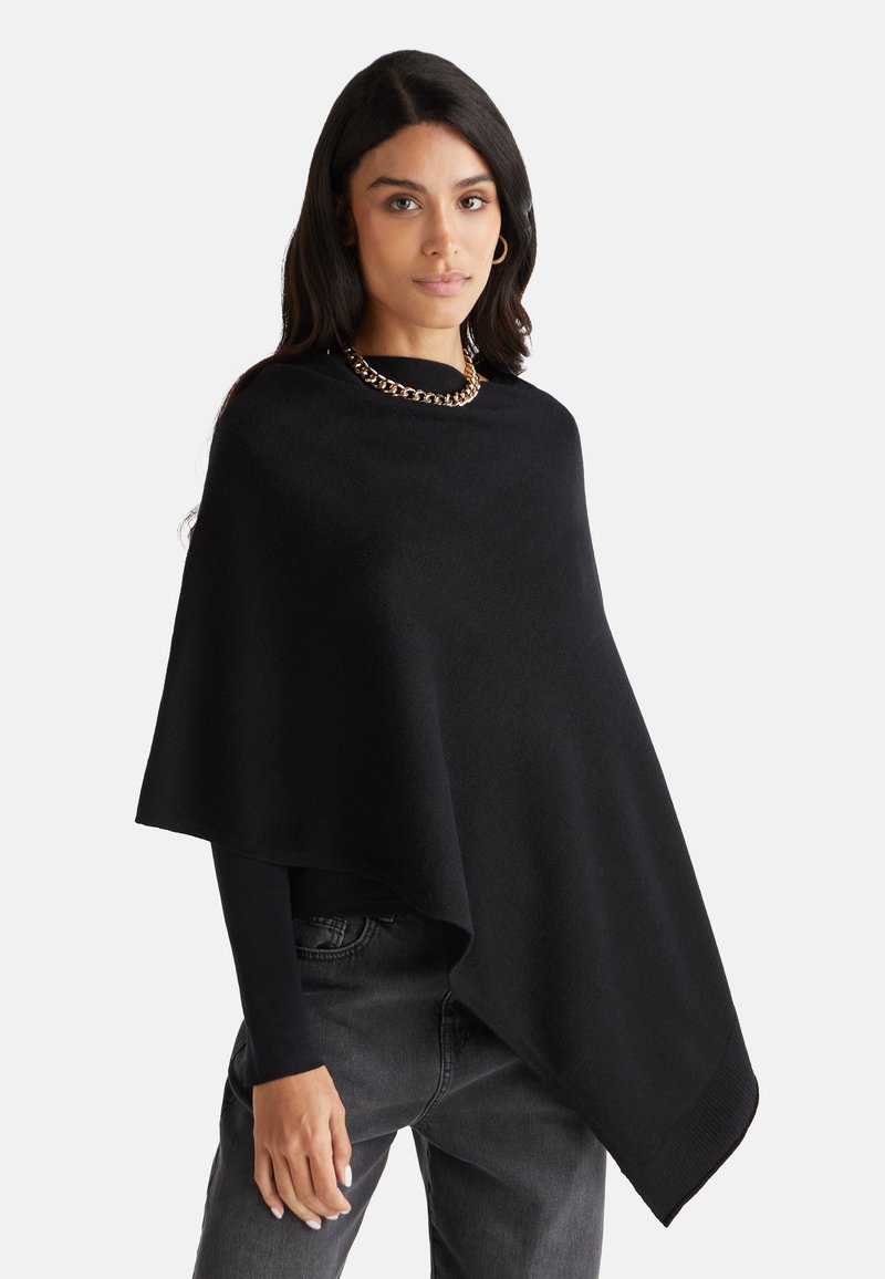 Černý pončo vyrobený z měkké látky, s kulatým výstřihem a asymetrickým lemem. Ozdobené robustním zlatým řetízkem.