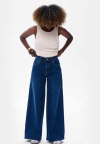 Szerokie, ciemnoniebieskie dżinsy z wysokim stanem, z frontowymi kieszeniami, zapięciem na guzik oraz ogólnym denimu teksturą.