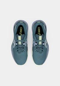 Ζευγάρι τυρκουάζ παπούτσια για τρέξιμο Asics με κορδόνια, λευκές σόλες και κίτρινες λεπτομέρειες με λογότυπο, απεικονιζόμενα από πάνω σε λευκό φόντο.