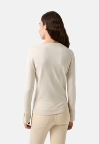Helle beige, figurbetonte Strickjacke mit langen Ärmeln, geripptem Ausschnitt und Bündchen. Weiche Textur; zeichnet sich durch ein sauberes, minimalistisches Design ohne Muster aus.