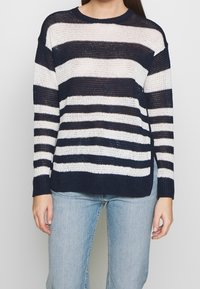 Striped knit sweater in navy and white. Features a round neckline, long sleeves, and a loose fit. Texture is lightweight and slightly airy.