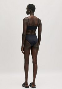 Schwarzes Bikini-Set mit einem taillierten Oberteil mit verstellbaren Trägern und hochgeschnittenen Unterteilen. Glattes, leichtes Material mit minimalistischer Gestaltung.