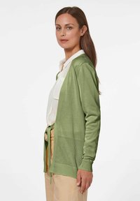 Groene gebreide cardigan met lange mouwen, gelaagd ontwerp, open voorkant en striksluiting. Bevat een gaasgedeelte aan de onderrand voor textuurcontrast.