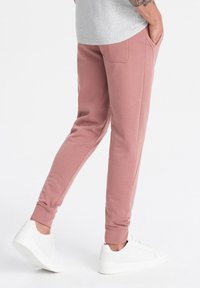 Helle rosa Jogginghose aus weichem Stoff, mit schlanker Passform, gerippten Bündchen und seitlichen Taschen, kombiniert mit weißen Sneakern.
