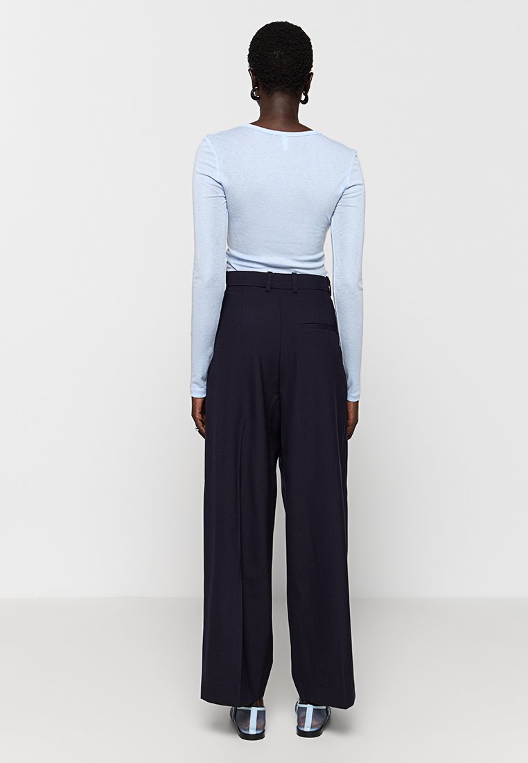 Jasnoniebieska bluzka z długim rękawem w połączeniu z wysokimi, luźnymi ciemnymi spodniami. Charakteryzuje się subtelną teksturą i dopasowanym krojem.