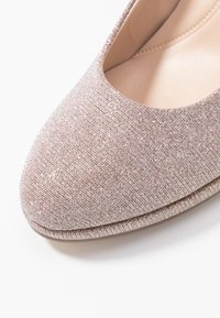 Błyszczący różowy płaski but z okrągłym nosem, teksturowana powierzchnia z materiału i gładka podszewka wewnętrzna. Udekorowany subtelnym połyskiem.