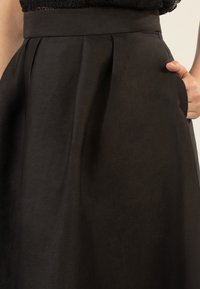 Jupe noire en tissu texturé, avec une taille ajustée, des poches latérales et un design plissé pour plus de volume.