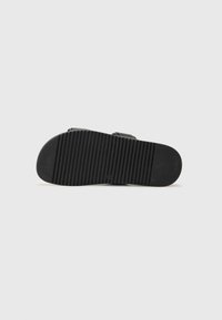 Black rubber sandal sole with a textured, ribbed pattern for grip. Curved shape with an oval toe area and defined arch support.