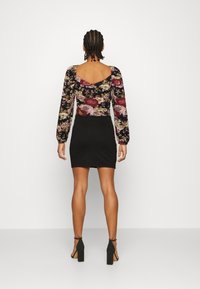 Top floreale a maniche lunghe con scollo a V profondo, abbinato a una minigonna nera fitted. Tessuto morbido con una miscela di colori bordeaux, rosa e oro.