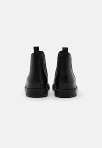 Μαύρες δερμάτινες μπότες ασφαλείας μέχρι τον αστράγαλο με λεία επιφάνεια, ελαστικές πλευρικές επενδύσεις και χειρολαβές, με στρογγυλή μύτη και καουτσούκ σόλα.