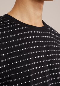 Close-up van de nek en schouder die een zwarte gebreide trui draagt met dunne horizontale witte strepen en een ronde hals