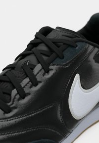 Μαύρο δερμάτινο αθλητικό παπούτσι με γυαλιστερό φινίρισμα, διαθέτει μαύρα κορδόνια, λευκό λογότυπο Nike swoosh και υφή πινακίδα σε μαύρο χρώμα, σχεδιασμένο για άνεση.