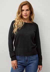 Schwarzer gestrickter Pullover mit Rundhalsausschnitt und gerippten Bündchen, kombiniert mit blauen Denim-Jeans. Einfaches Design, weiche Textur, mittellange Passform.