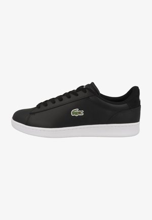 Baskets basses noires avec semelle blanche, lacets noirs et logo crocodile vert sur le côté, vues de l'extérieur.