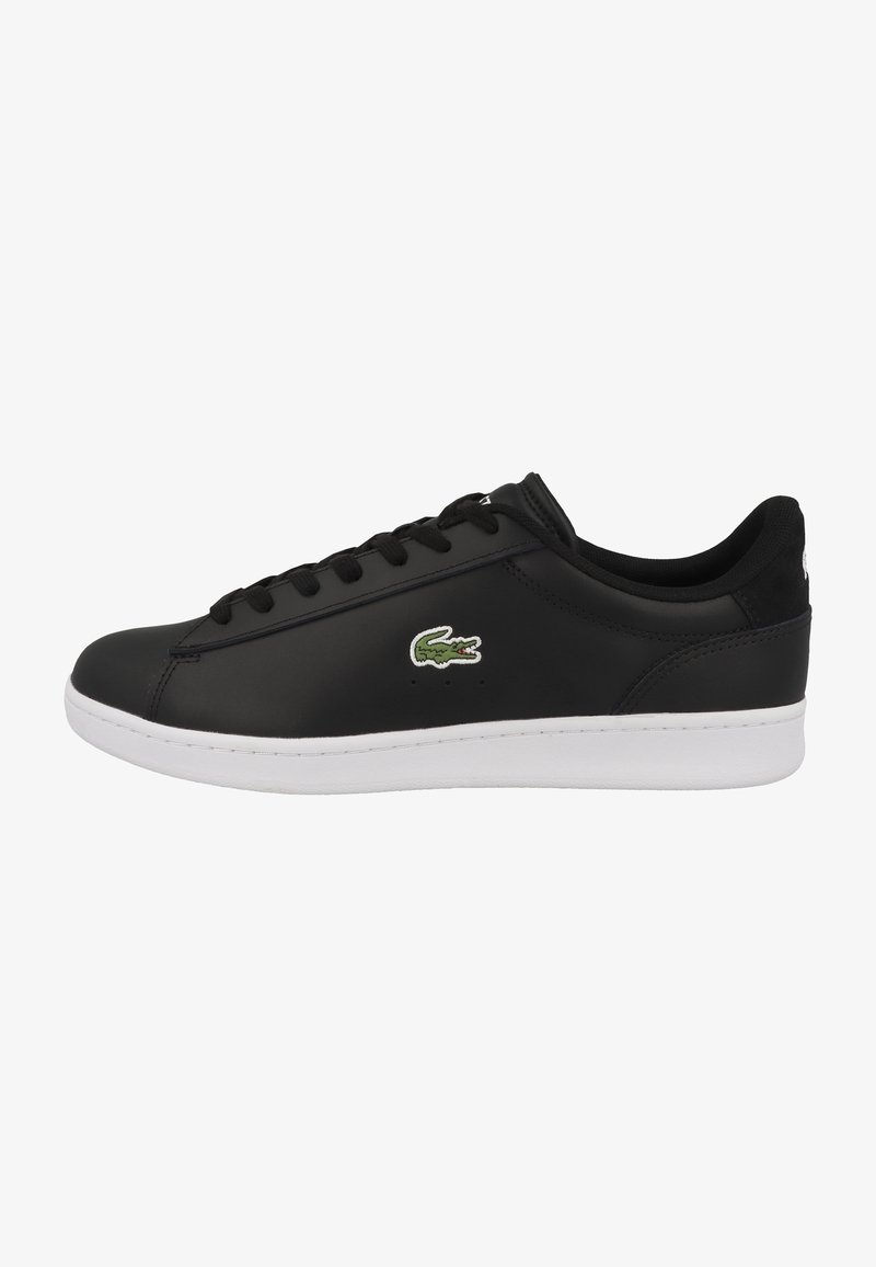 Baskets basses noires avec semelle blanche, lacets noirs et logo crocodile vert sur le côté, vues de l'extérieur.