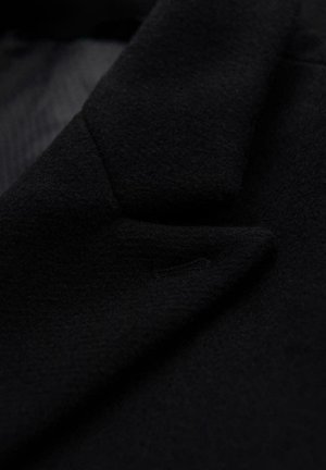 Schwarzer Wollmantelstoff mit glatter Textur, ausgestattet mit einem strukturierten Kragen und einem kleinen, dezenten Taschendetail am Revers.