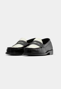 Sabrinas de couro preto com detalhes em couro branco, apresentando uma costura ao estilo mocassim e duas correias decorativas na parte superior.