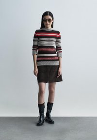 Sweter z dzianiny w poziome paski w kolorze szarym, czerwonym i czarnym; zestawiony z brązową mini spódnicą zamszową i czarnymi kozakami za kolano.