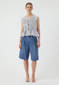 Haut peplum rayé noir et blanc avec taille froncée, assorti à un short en denim bleu mi-cuisse et à des sandales ouvertes argentées.