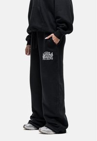Zwarte sweatpants van zacht materiaal, met een trekkoord in de taille en een witte graphic "GOOD FOR NOTHING" op het linkerbeen.