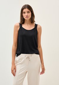 Top nero senza maniche con dettagli delle spalle sfilacciati, realizzato in un tessuto morbido. Abbinato a pantaloni beige chiaro con coulisse, caratterizzati da cuciture frontali.