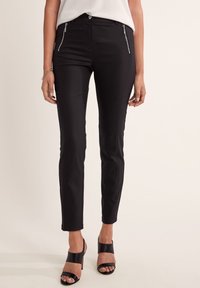 Zwarte slim-fit broek met stijlvolle ritssluitingen aan de voorkant, vervaardigd uit soepele stof, met een klassieke tailleband en een getailleerde pasvorm.