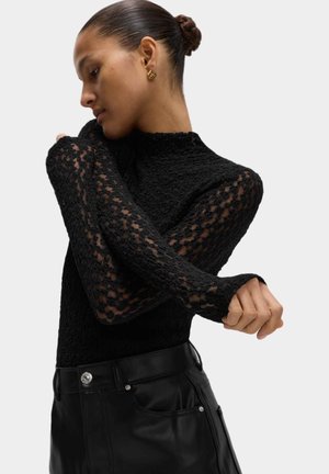 Top negro de manga larga con tejido texturizado y mangas de encaje transparente, combinado con pantalones de cuero negro de cintura alta con acentos plateados.