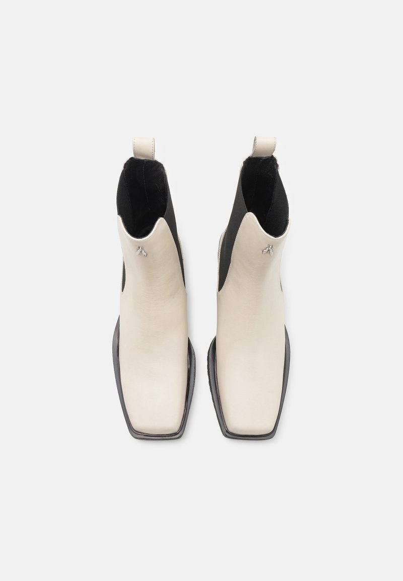 Białe skórzane botki za kostkę z czarnymi elastycznymi bokami, kwadratowymi noskami i płaską czarną podeszwą. Na cholewce widoczny jest mały srebrny akcent.