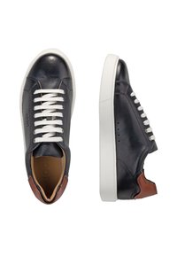 Mörkblå läderskor med vita snören, bruna hälaccenter och en vit gummisula. Texturerad yta och logotyp präglad på sidan.