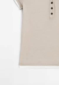 Polo beige côtelé à manches courtes, avec une patte de boutonnage comportant quatre boutons noirs et une bordure blanche à l'ourlet.