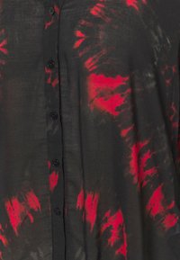 Chemise noire à boutons avec un motif tie-dye rouge et gris foncé, montrant la texture du tissu et un gros plan des boutons sur le devant.