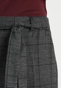 Pantalons à carreaux gris en tissu texturé, taille haute, avec une ceinture en tissu nouée à l'avant. Motif de check noir et blanc subtil.