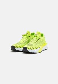 Limegröna träningsskor med ett andningsbart överdel av mesh, vadderad krage och en vit mellansula med svarta gummidetaljer och spår.