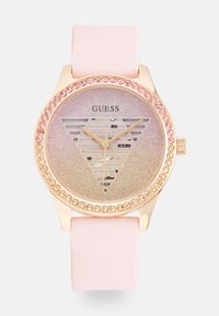 Gullfarget klokke med rosa silikonrem. Glitrende gradient urskive med trekantdesign og krystalldetaljer rundt bezel.