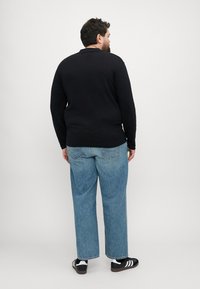Svart langermet skjorte med krage, kombinert med lyseblå løse jeans og svarte joggesko med hvite striper, sett fra baksiden.