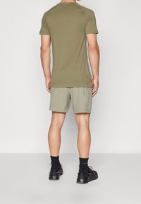 Camisa de manga corta verde oliva y pantalones cortos verde claro, mostrados desde atrás. La camisa presenta un escote redondeado; los pantalones cortos son hasta medio muslo.