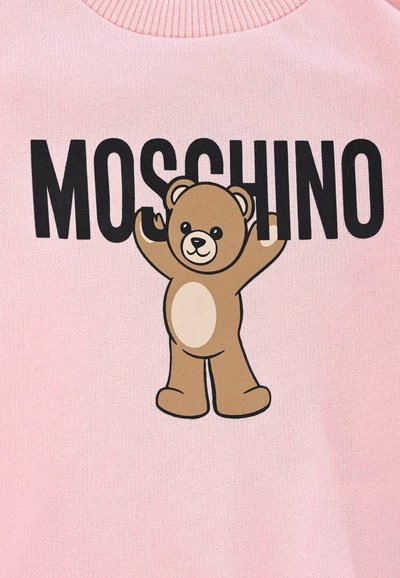 Sweat-shirt rose avec un ours en bande dessinée marron, les bras levés, et le mot "MOSCHINO" en lettres noires en gras. Tissu doux.