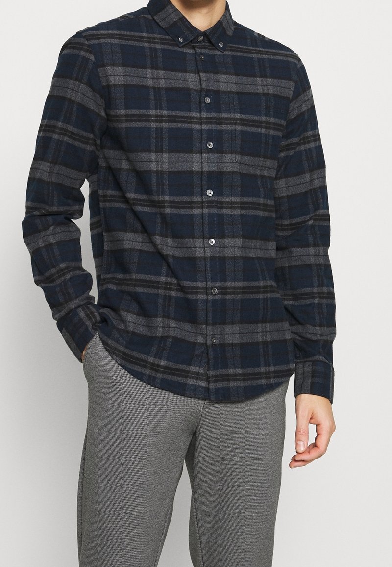 Camicia a quadri navy e grigia, realizzata in tessuto flanella, con colletto, maniche lunghe e vestibilità aderente, dotata di chiusura frontale con bottoni.
