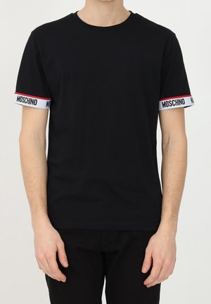 Man wearing plain black short-sleeve T-shirt with white and red trim on sleeves featuring "MOSCHINO" text.